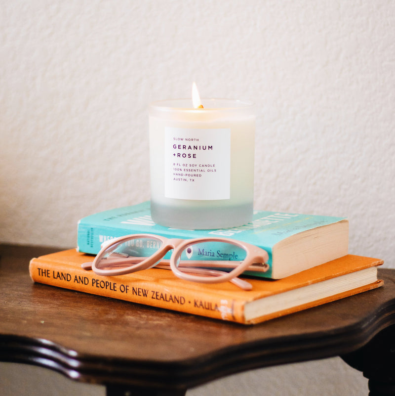 Lit soy wax candle in 8 ounce clear frosted tumbler on top of books. By Slow North
