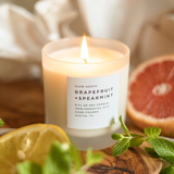 Lit Grapefruit + Spearmint soy wax candle in 8 ounce clear frosted tumbler near a grapefruit on a table