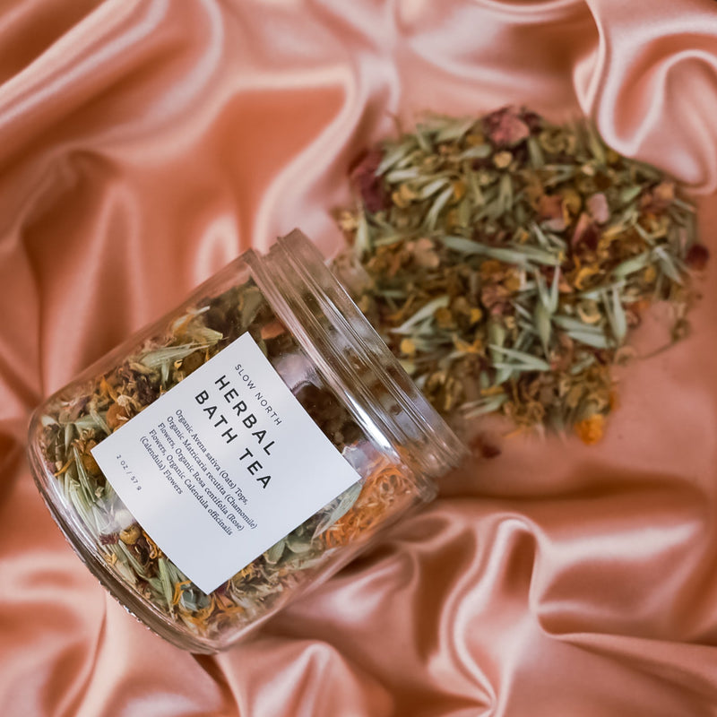 Herbal Bath Tea - 2 ounce in glass jar, spilling from jar on pink silk fabric. By Slow North 