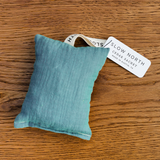 A close-up of a rectangle natural cotton herbal sachet that is made with a teal cotton cloth and filled with cedar chips.