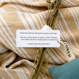 A close-up of rectangle lavender + cedar sachets tag TEXT: Filled with dried lavender buds & aromatic cedar chips. Slip into a clothes drawer or hang in a closet to freshen your clothes and linens for insect-repelling benefits. Gently squeeze to reactivate.