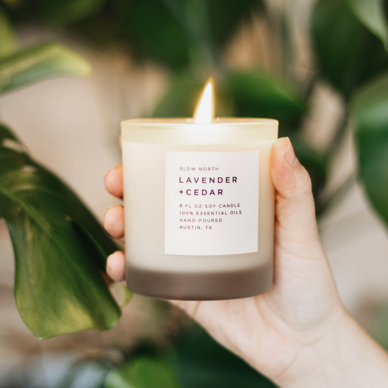 Hand holding a lit soy wax candle in 8 ounce clear frosted tumbler by Slow North