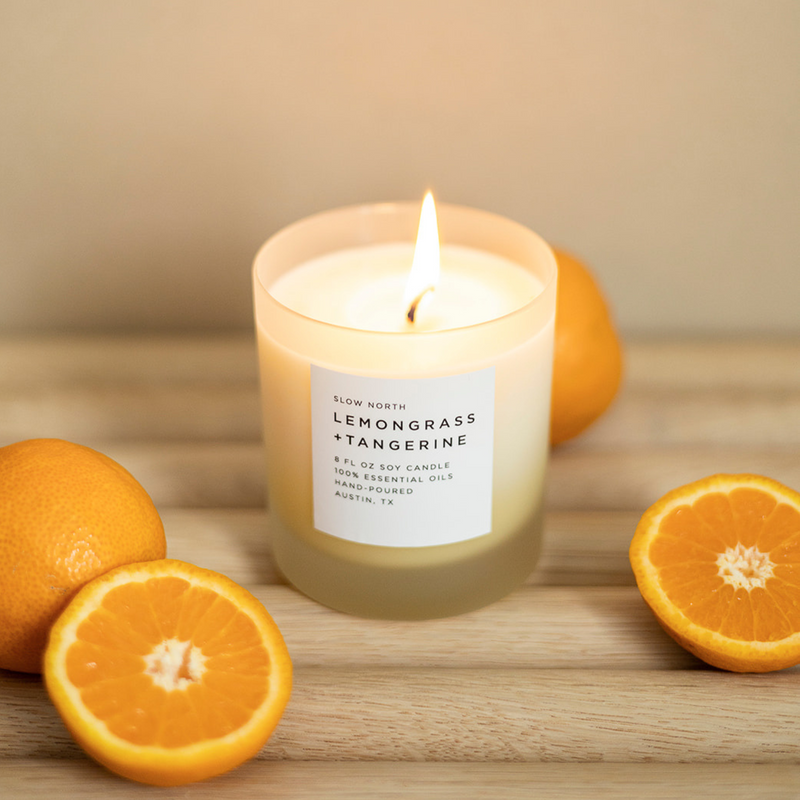 Lit Lemongrass + tangerine soy wax candle in 8 ounce clear frosted tumbler surrounded by tangerines