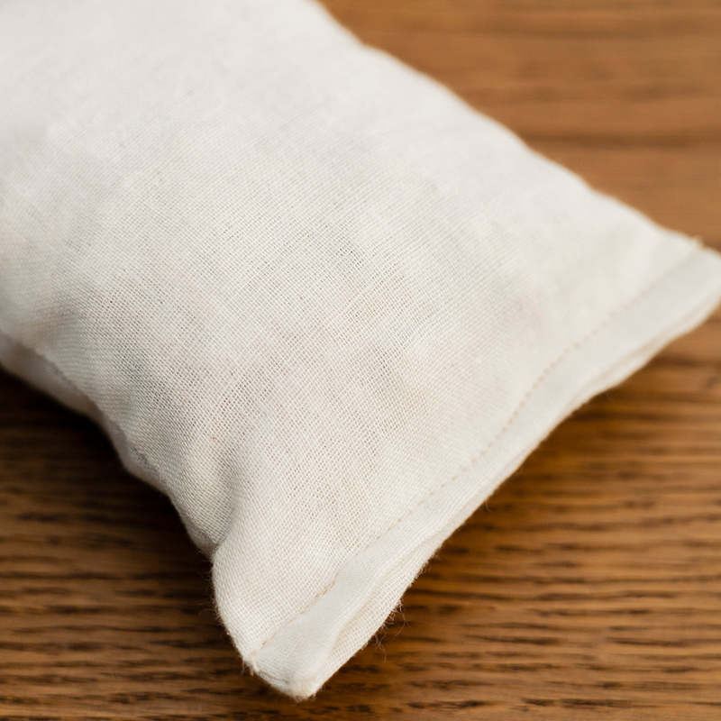A close-up of a rectangle natural cotton herbal sachet that is an off-white cloth and filled with cedar.