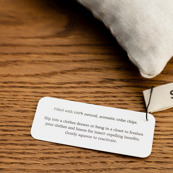 A close-up of rectangle cedar sachets tag TEXT: Filled with 100% natural, aromatic cedar chips.Slip into a clothes drawer or hang in a closet to freshen your clothes and linens for insect-repelling benefits. Gently squeeze to reactivate.