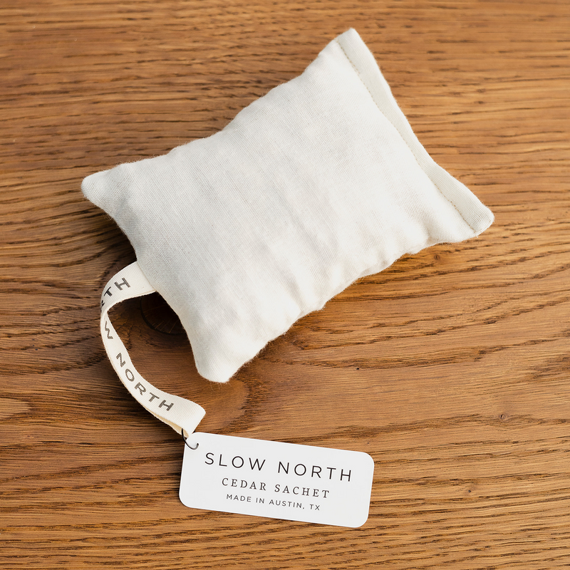 A close-up of a rectangle natural cotton herbal sachet that is an off-white cloth and filled with cedar chips.