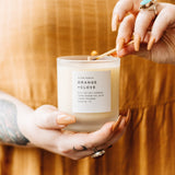 Woman's hands holding a matchstick and lighting a soy wax candle in 8 ounce clear frosted tumbler by Slow North